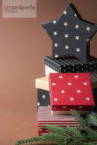 Christmas presents frame with a stack of red and black boxes with various designs and a star-shaped gift on top  on a brown background