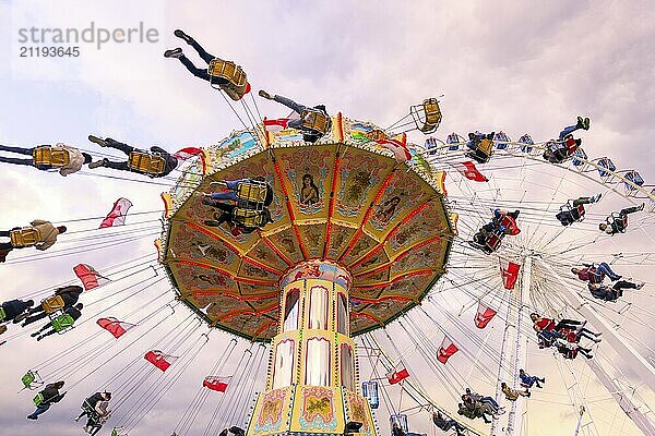 Kettenkarussell in Bewegung mit fröhlichen Menschen vor wolkigem Himmel  Riesenrad  Wellenflug  Cannstadter Volksfest  Stuttgart  Baden-Württemberg