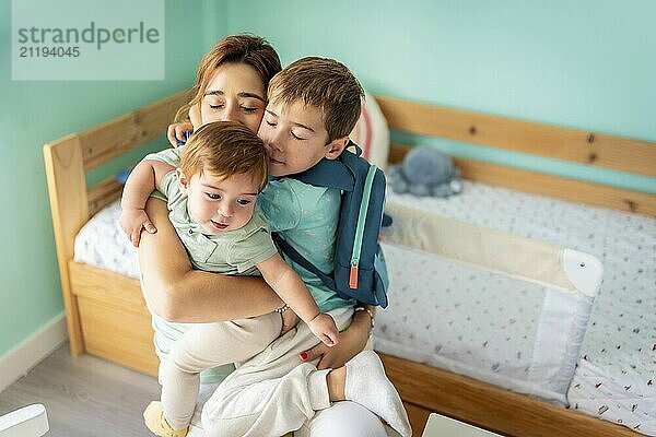 Happy family of three. Mother embracing boy and baby sitting in the bedroom