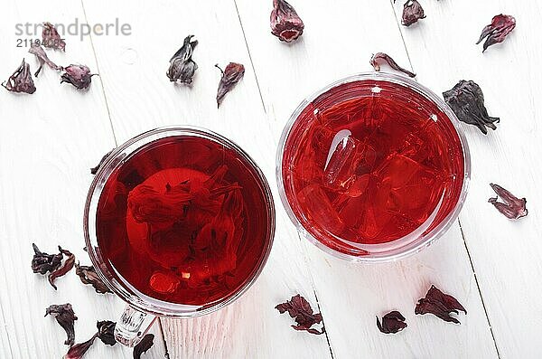 Top view at two tea cups with ice and dry hibiscus petals on white wooden table background