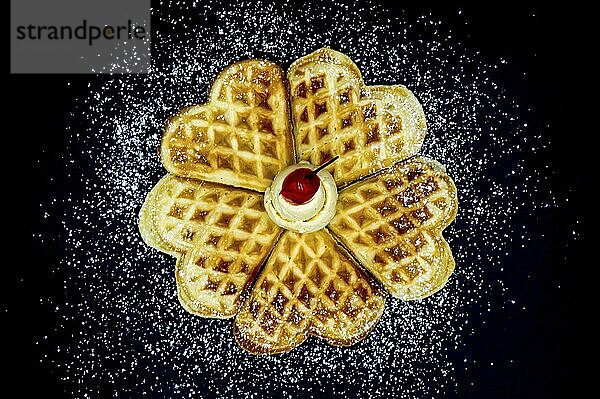 Homemade waffles with powdered sugar  a scoop of vanilla ice cream and a cherry on a black background  isolated image of food