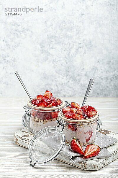 Parfait mit frischen Erdbeeren  Joghurt und knusprigem Müsli in transparenten Einmachgläsern auf weißem  rustikalem Holzhintergrund Schrägansicht  gesundes Frühstück oder leichtes Sommerdessert  Copy Space  Foodfotografie