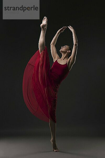 Beautiful girl in red chiffon dress dancing gracefully in dark room view