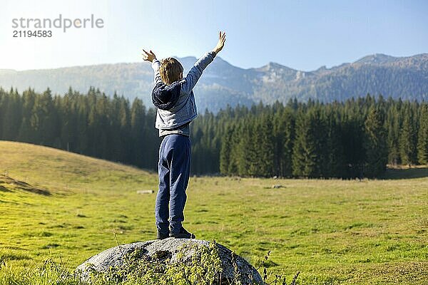 Happy boy child raising hands over clear sky. Hiking in nature on beautiful autumn day and enjoying the moment and view