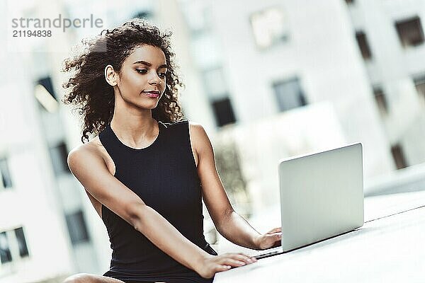 Young attractive Mixed-race girl with beautiful afro hair who is smiling looking at her laptop screen during video call. Young woman using laptop