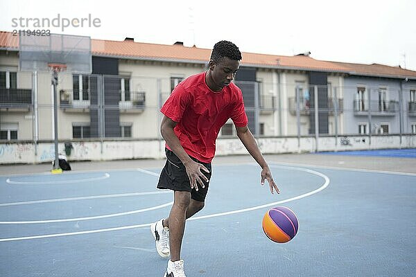 Full length photo of a sportive young african man dribbling at a basketball court