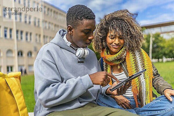 Smiling multiethnic young couple using tablet sitting outside the university campus