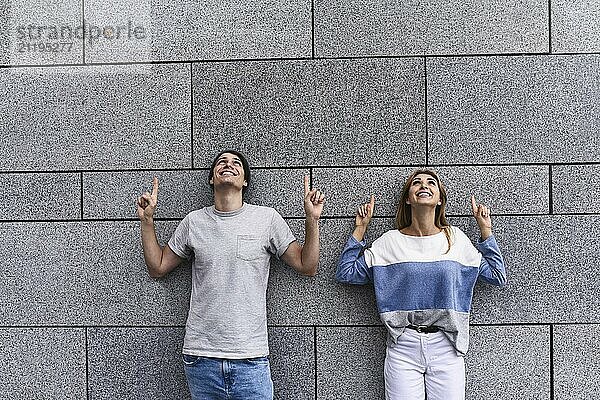 Cheerful couple at the street  show a big sale  or nice offer. Advertise concept. People  travel and tourism  on city street and couple show with their fingers something over gray wall background