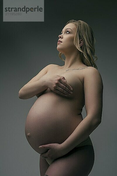 Pregnant blonde in the nude cropped shot against gray wall