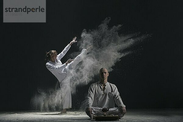 Two male doing yoga in a white dust cloud in dark room full-length view