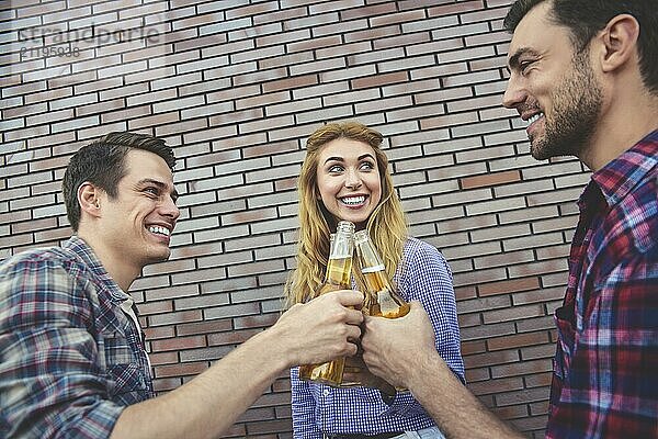 The three happy friends enjoying with beer on a brown brick wall background