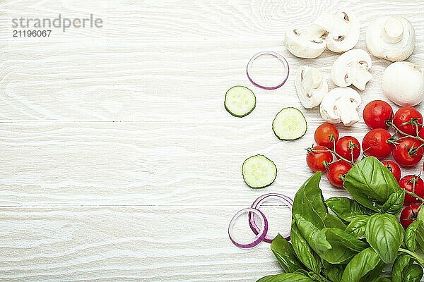 Food cooking background: fresh ingredients basil  cherry tomatoes  mushrooms  cut cucumber and onion on white wooden background top view. Meal preparing template  space for text  food photography