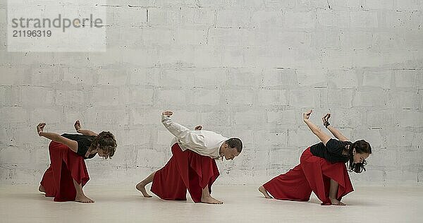 Two women and their male trainer doing yoga exercises view against brick wall