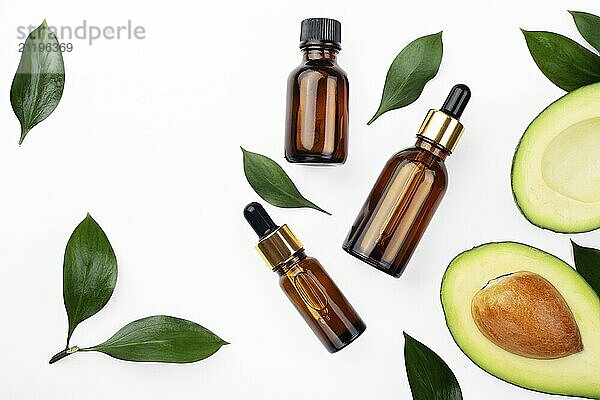 Dropper bottles with fresh ripe avocado and essential oil on white table flat lay