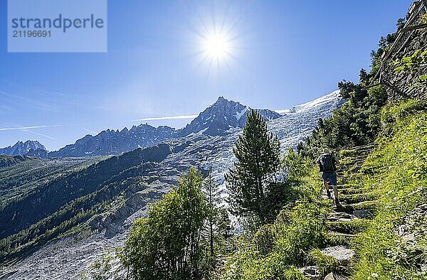 Hiker on hiking trail La Jonction  view of glacier Glacier des Bossons with sun star  behind summit of Aiguille du Midi  Chamonix  Haute-Savoie  France  Europe