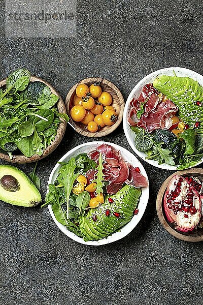 Food  Low carbs bowl. Fresh salad with green spinach  rucola  avocado an ham serrano in white bowl  gray background  top view