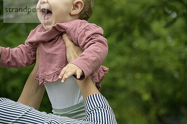 Ein Baby wird lachend in die Luft gehoben  umgeben von grüner Natur