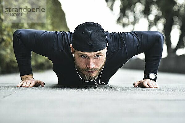 Young bearded sportsman makes workout in a park  doing a series of push ups outdoor