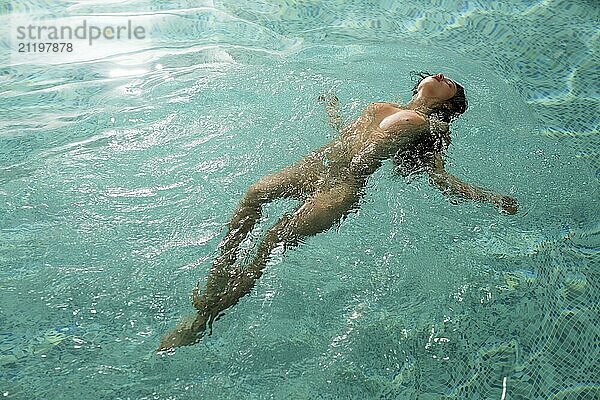 Nude girl relaxing in a swimming pool full-length view