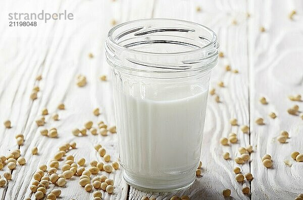 Non-dairy alternative Soy milk or yogurt in mason jar on white wooden table with soybeans aside