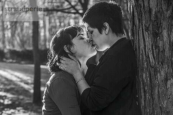 LGBT couple of women sharing a passionate kiss against a tree in black and white