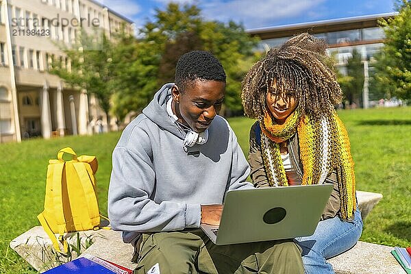 African student and latin female colleague using laptop sitting outside the campus