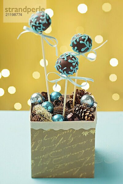 Chocolate cake pops garnished with turquoise icing sticking in nice Christmas gift box. Very shallow depth of field with Christmas lights in the background