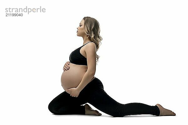 Young pregnant woman in black sportswear doing fitness sitting in a split isolated profile shot