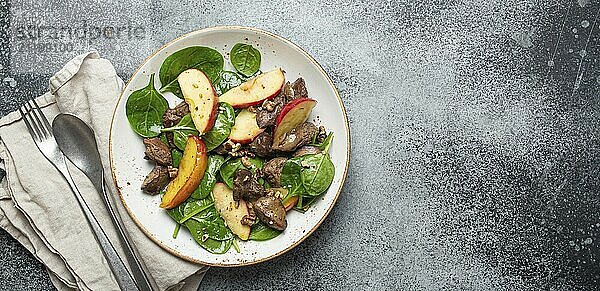 Gesunder Salat mit eisenreichen Zutaten Hühnerleber  Äpfel  frischer Spinat und Walnüsse auf weißem Keramikteller  grauer rustikaler Steinhintergrund Draufsicht Kopierraum  Foodfotografie