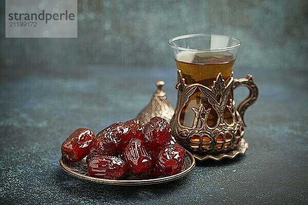 Fastenbrechen mit getrockneten Datteln während des Ramadan Kareem  Iftar Mahlzeit mit Datteln und arabischem Tee im traditionellen Glas  Blickwinkel auf rustikalem blauen Hintergrund. Muslimisches Festmahl  Foodfotografie