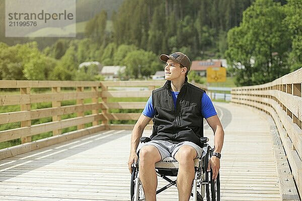 Disabled young man on a wheelchair on a wooden bridge path enjoying in nature looking at beautiful view