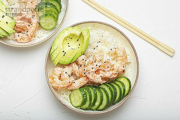 Two white ceramic bowls with rice  shrimps  avocado  vegetables and sesame seeds and wooden sticks on white concrete stone background top view. Healthy asian style poke bowl