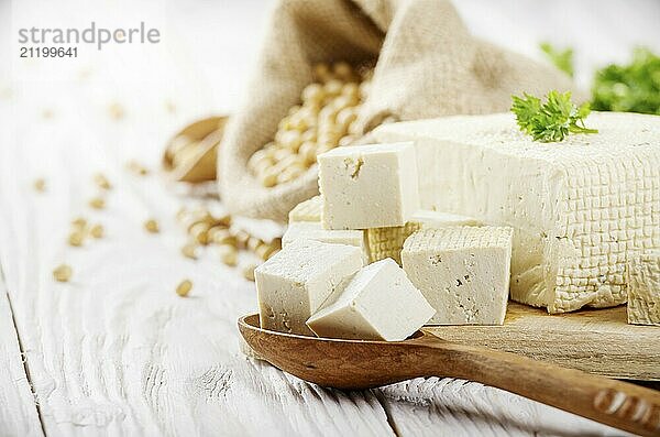 Soy Bean curd tofu on cutting board and in hemp sack on white wooden kitchen table. Space for text