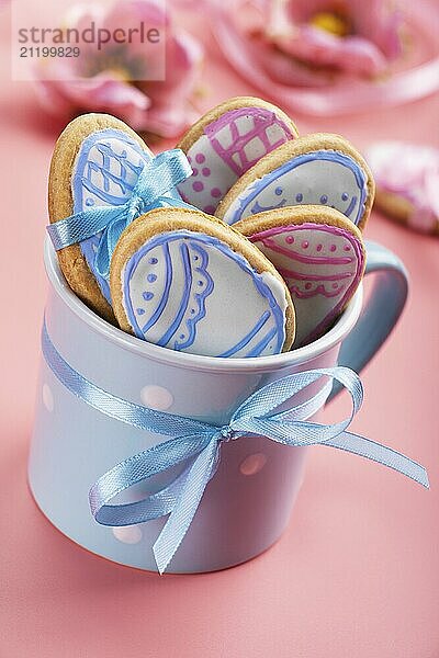 Ostern Backen Hintergrund der gefrosteten Cookies in Form von Ei in blauen Becher auf rosa Hintergrund