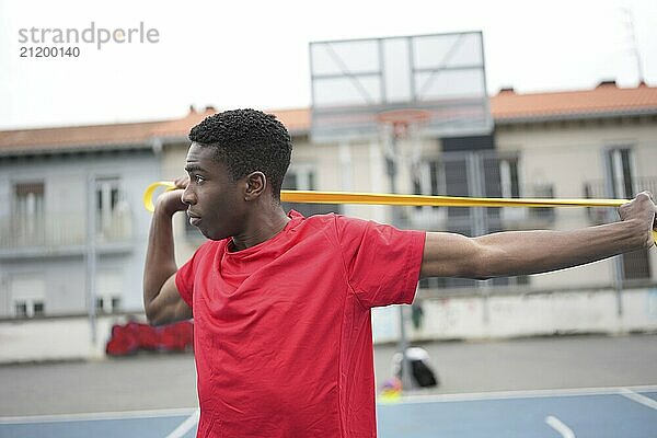 Concentrated african man warming up using elastic band in an outdoor urban basketball court