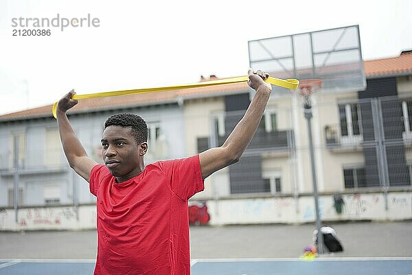 Horizontal photo with copy space of a young african man warming up and stretching using an elastic resistance band in an outdoor basketball court