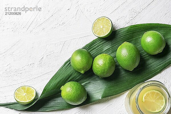 Bunch of limes on a big green leaf and a jar with freshly squeezed lime juice  on a white background. Above view with copy space. Detox context