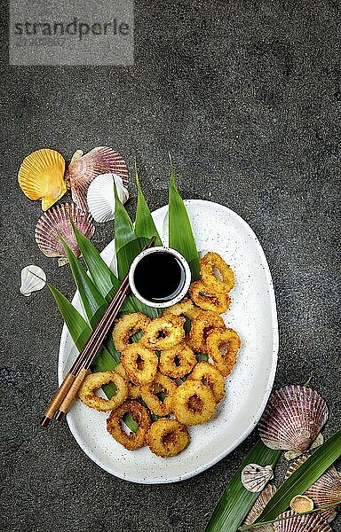 Food  Food  Fried squids rings on white plate decorated with tropical leaves  gray concrete background  top view