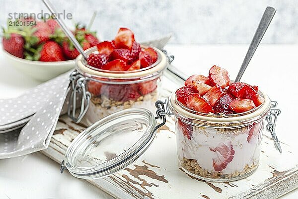 Parfait mit frischen Erdbeeren  Joghurt und knusprigem Müsli in durchsichtigen Einmachgläsern auf weißem  rustikalem Holzhintergrund aus der Vogelperspektive  gesundes Frühstück oder leichtes Sommerfruchtdessert  Foodfotografie  food photography  food photography