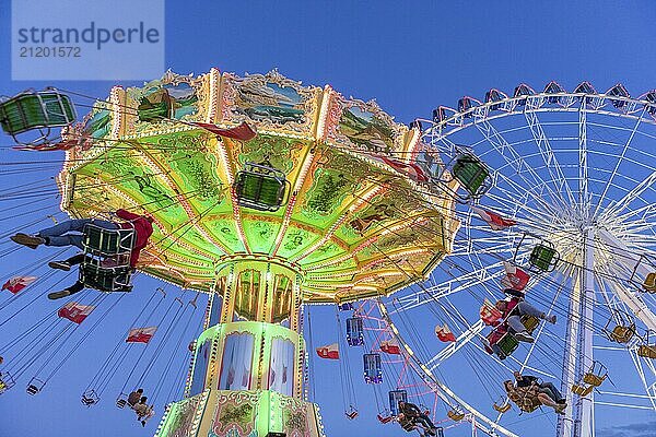 Beleuchtetes Kettenkarussell und Riesenrad bei Nacht mit fröhlichen Menschen  Jahrmarkt  Wellenflug  Cannstadter Volksfest  Stuttgart-Bad Cannstsdt  Baden-Württemberg