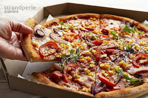 Human caucasian hand takes slice of large pizza from carton box on white wooden table