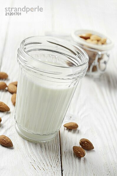 Milk or yogurt in mason jar on white wooden table with almonds in airtight conainer aside