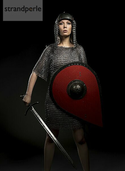 Sexy female wearing viking helmet and hauberg with a sword and shield isolated view on black background