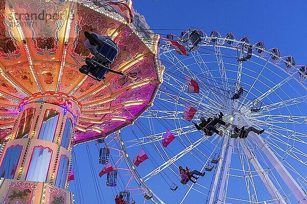 Beleuchtetes Kettenkarussell und Riesenrad bei Nacht mit fröhlichen Menschen  Jahrmarkt  Wellenflug  Cannstadter Volksfest  Stuttgart-Bad Cannstsdt  Baden-Württemberg