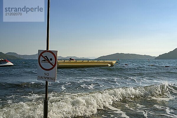 Turkish sea shore washed by waves and the sign no swimming on the foreground shot