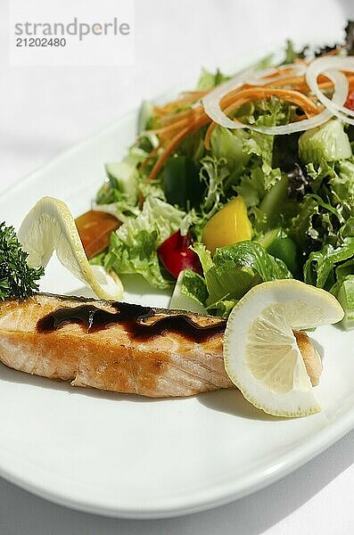 Organic mixed vegetable salad with salmon fillet and balsamic vinaigrette on white restaurant table