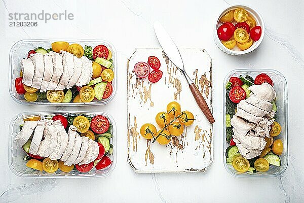 Gesunde Mahlzeit Vorbereitung für das Mittagessen  Diät gekochtes Hühnerfilet mit Gemüse Salat in Lunch Boxen Container Draufsicht auf weißen Marmor Küchentisch Hintergrund mit Messer und Schneidebrett  Lebensmittel Fotografie  food photography