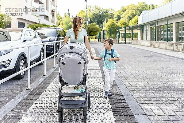 Full length photo of a happy caucasian mother and son pushing baby carriage going home after school