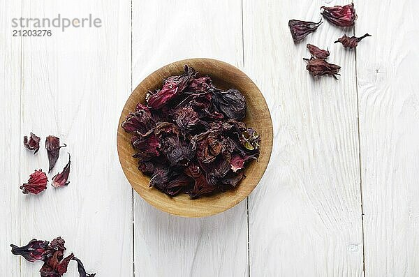 Top view at wooden bowl of dry hibiscus petals on white background