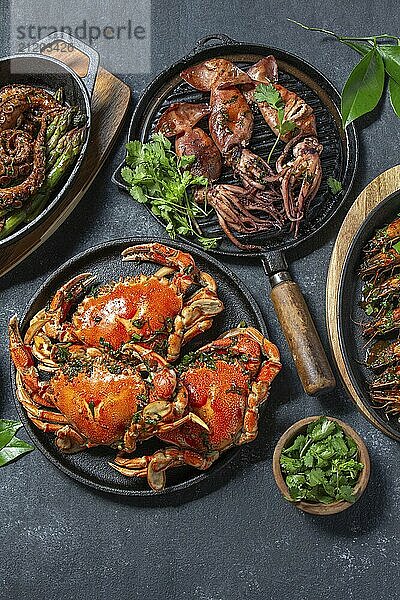 Food  Food  Set of Seafood Dishes. Crabs  octopus  squids and tiger shrimps on cast iron pans and plates on a black background. Top view